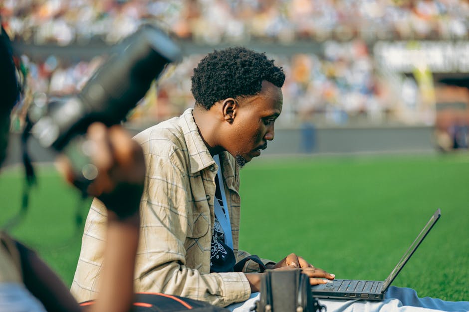 Photographer using a laptop at an outdoor event on a sunny day.